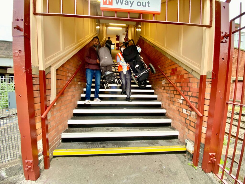 Shows passengers with pushchairs ascending the stairs at Small Heath station.